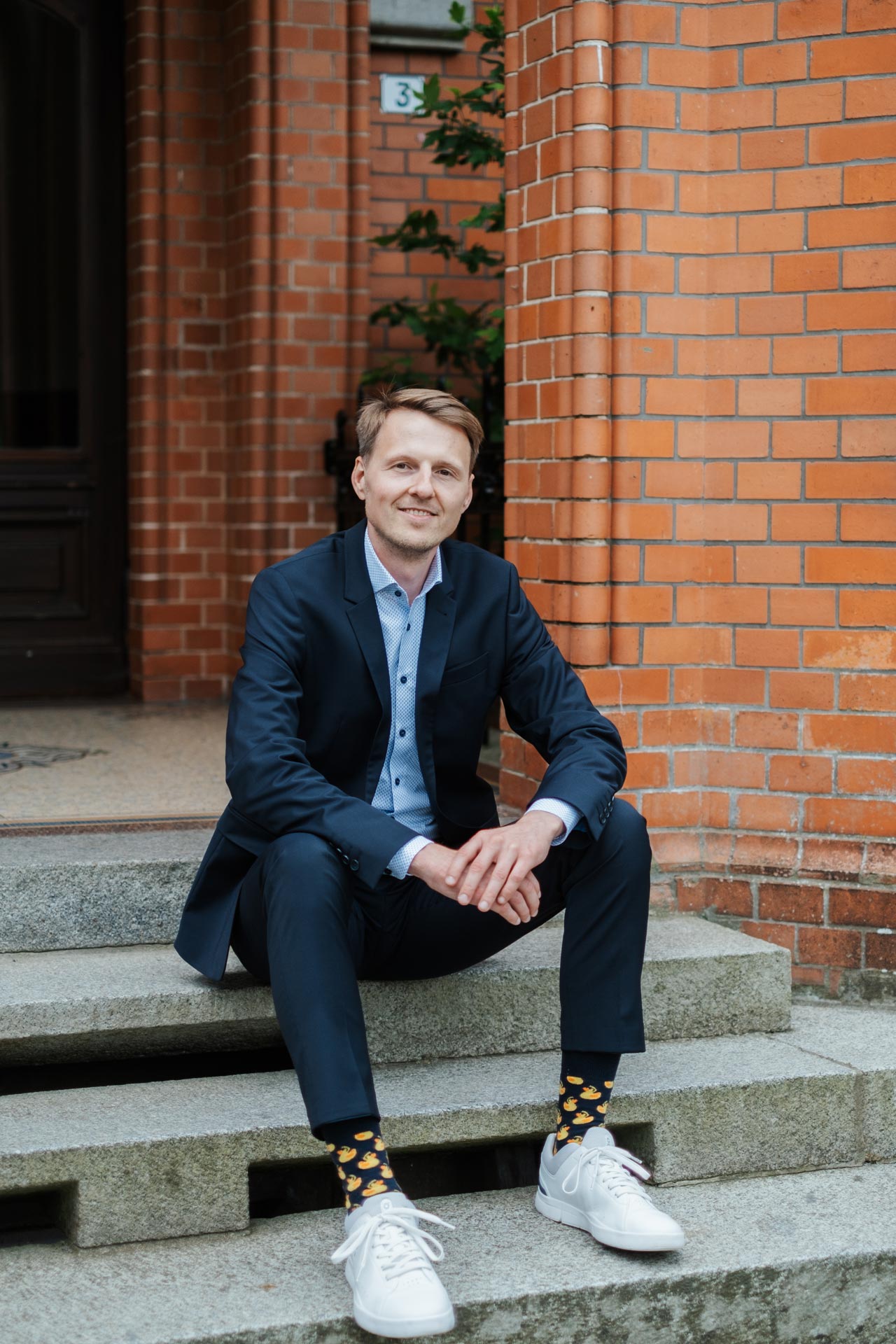 IT-Professional Dennis Quas sitzt auf Steintreppen vor einem verklinkerten Gebäude.